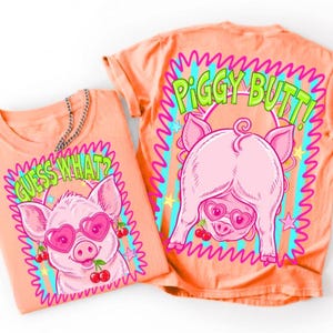 May include: A peach-colored t-shirt featuring a graphic of a pig wearing heart-shaped sunglasses and holding cherries. The front displays the text "GUESS WHAT?" and the back displays the text "PIGGY BUTT!" with a neon-colored border design.