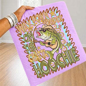 May include: A light purple blanket featuring a cartoon bass fish wearing a cowboy hat and sunglasses, playing a guitar. The blanket has the text "WAY DOWN YONDER ON THE CHATTA HOOCHIE" in a wavy design.