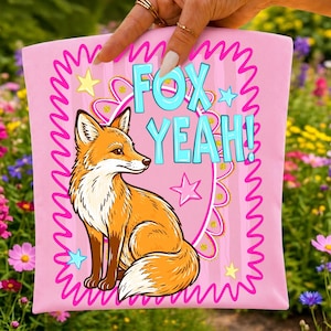 Op de afbeelding: Een roze stoffen vierkant met een centrale illustratie van een oranje en witte vos. De tekst "FOX YEAH!" staat in lichtblauwe letters boven de vos gedrukt. Het ontwerp bevat een roze geschulpte rand en verschillende gele en blauwe sterren.