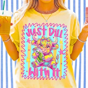 Puede incluir: Una camiseta amarilla con un gr&aacute;fico colorido de una vaca de las Highlands sosteniendo un frasco de pepinillos. El texto "JUST DILL WITH IT" est&aacute; impreso en rosa sobre y debajo de la vaca. El dise&ntilde;o est&aacute; enmarcado por un borde rosa ondulado.