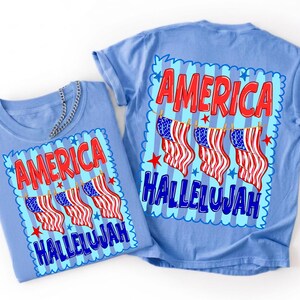 Puede incluir: Dos camisetas azul claro con un estampado gr&aacute;fico que incluye el texto rojo AMERICA y el texto azul HALLELUJAH. El dise&ntilde;o muestra tres banderas estadounidenses colgadas de un tendedero sobre un fondo de rayas azul claro con estrellas.