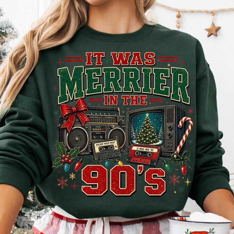 Może przedstawiać: Ciemnozielona bluza z długim rękawem z nadrukiem graficznym i napisem IT WAS MERRIER IN THE 90'S. Wz&oacute;r przedstawia radiomagnetofon z czerwoną kokardą, telewizor w stylu vintage z choinką oraz dwie kasety magnetofonowe.