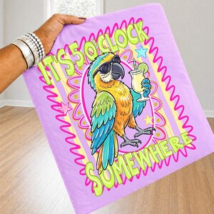 May include: A lavender blanket featuring a cartoon parrot wearing sunglasses and holding a cocktail. The text "IT'S 5 O'CLOCK SOMEWHERE" is displayed in green and pink. The parrot has blue, yellow, and orange feathers.