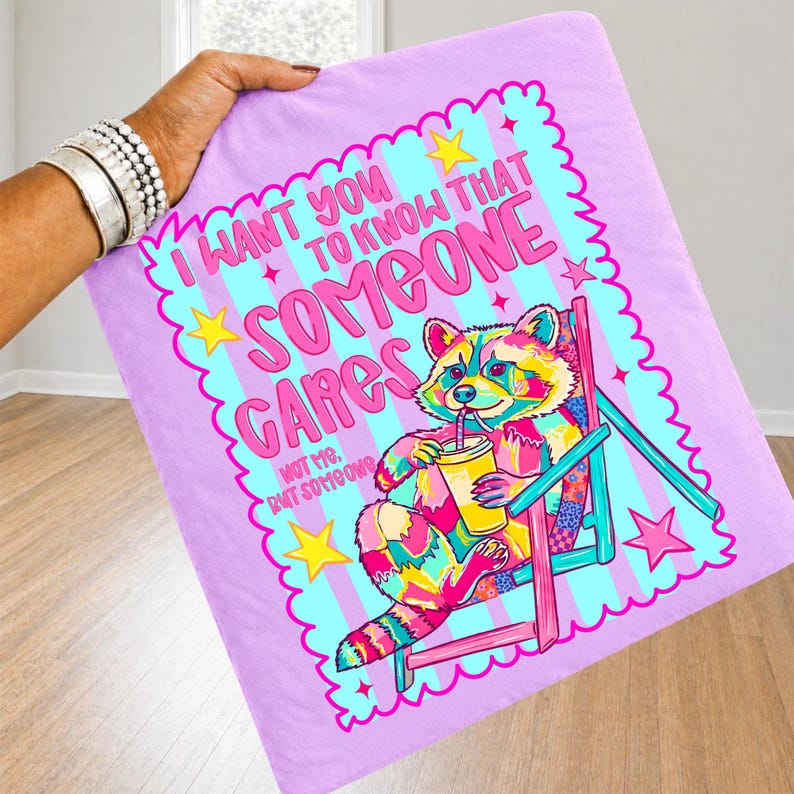 K&ouml;nnte beinhalten: Ein hellviolettes Stoffquadrat mit einem bunten Waschb&auml;ren, der in einem rosa Stuhl sitzt und ein gelbes Getr&auml;nk h&auml;lt. Der Text lautet: I WANT YOU TO KNOW THAT SOMEONE CARES, NOT ME, BUT SOMEONE. Das Design enth&auml;lt gelbe Sterne und einen gewellten Rand.