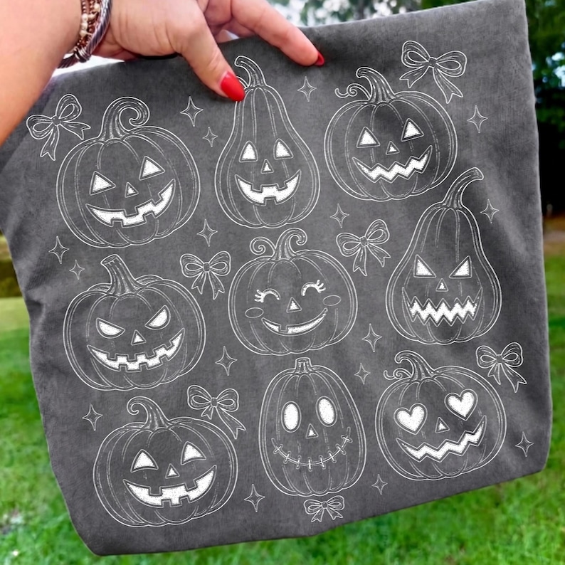 May include: A dark grey fabric tote bag featuring a white line art pattern of various jack-o'-lanterns with different facial expressions, including smiling, heart-shaped eyes, and jagged teeth, interspersed with small decorative bows and stars.