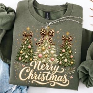 Peut inclure: Un sweat-shirt &agrave; col rond vert olive orn&eacute; d'un motif repr&eacute;sentant trois sapins de No&euml;l d&eacute;cor&eacute;s de boules dor&eacute;es et roses, surmont&eacute;s de n&oelig;uds &agrave; imprim&eacute; l&eacute;opard. Le texte Merry Christmas est &eacute;crit en lettres cursives cr&egrave;me en dessous.