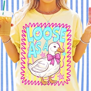 K&ouml;nnte beinhalten: Ein hellgelbes T-Shirt mit einer Grafik einer wei&szlig;en Ente, die eine rosa Schleife tr&auml;gt. Der Text LOOSE AS A ist in hellblauen Buchstaben gedruckt. Das Design ist von einem leuchtend rosa, wellenf&ouml;rmigen Rand mit gelben Streifen umgeben.