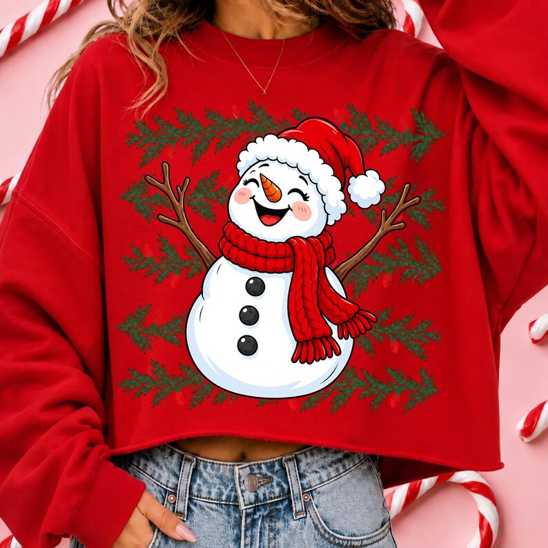 Puede incluir: Una sudadera roja de manga larga con un gr&aacute;fico central de un mu&ntilde;eco de nieve sonriente que lleva un gorro de Pap&aacute; Noel rojo y una bufanda de punto roja. El mu&ntilde;eco tiene una nariz de zanahoria, tres botones negros y ramas de pino verdes.