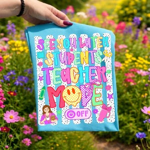 K&ouml;nnte beinhalten: Ein hellblaues T-Shirt mit einer bunten Grafik und dem Text "SEE YOU LATER STUDENTS TEACHER MODE OFF". Das Design zeigt ein gelbes Smiley-Gesicht, eine Lehrkraft, einen pinken Becher, einen gr&uuml;nen Stift und eine Schere auf wei&szlig; gestreiftem Grund.
