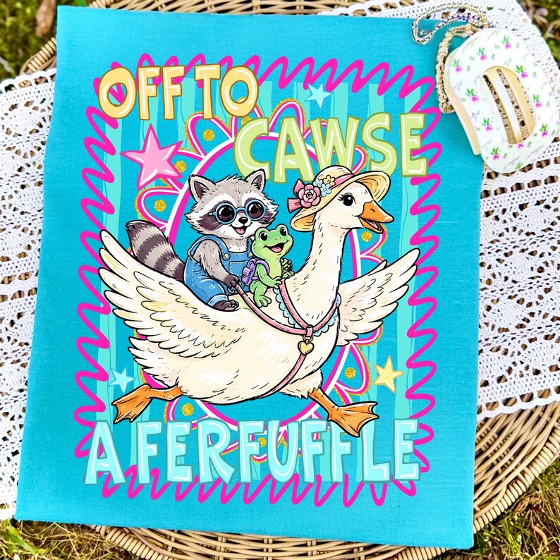 May include: A teal-colored graphic featuring a cartoon goose wearing a hat, carrying a raccoon and a frog. The text "OFF TO CAWSE A FERFUFFLE" is displayed in a playful font, surrounded by pink squiggly lines and stars. The design is on a square fabric.