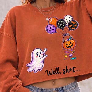 May include: A burnt orange long-sleeve sweatshirt featuring a graphic of a white ghost reaching toward a pumpkin basket held by a cluster of colorful balloons. The text "Well, sh*t..." is printed in black below the ghost and pumpkin illustration.