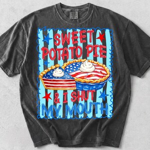 Op de afbeelding: Een antracietgrijs t-shirt met een afbeelding van twee taarten in Amerikaanse vlagstijl met toefjes slagroom. De tekst luidt SWEET POTATO PIE & I SHUT MY MOUTH, omringd door blauwe verticale strepen en rode en blauwe sterren op een geschulpte rand.