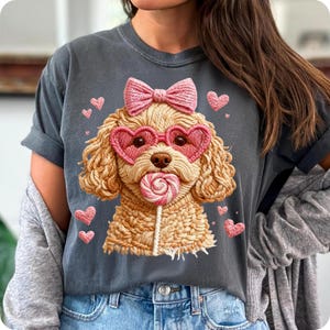 May include: Dark gray t-shirt featuring a cartoon poodle with heart-shaped sunglasses, a pink bow, and a lollipop. Pink hearts surround the poodle. The shirt has rolled-up sleeves and a casual fit.