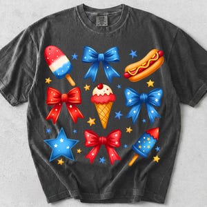 K&ouml;nnte beinhalten: Ein anthrazitfarbenes Kurzarm-T-Shirt mit einem grafischen Aufdruck aus roten, wei&szlig;en und blauen patriotischen Symbolen, darunter Schleifen, ein Eis am Stiel, ein Hotdog, eine Eist&uuml;te, eine Feuerwerksrakete und kleine, &uuml;ber die Vorderseite verteilte Sterne.