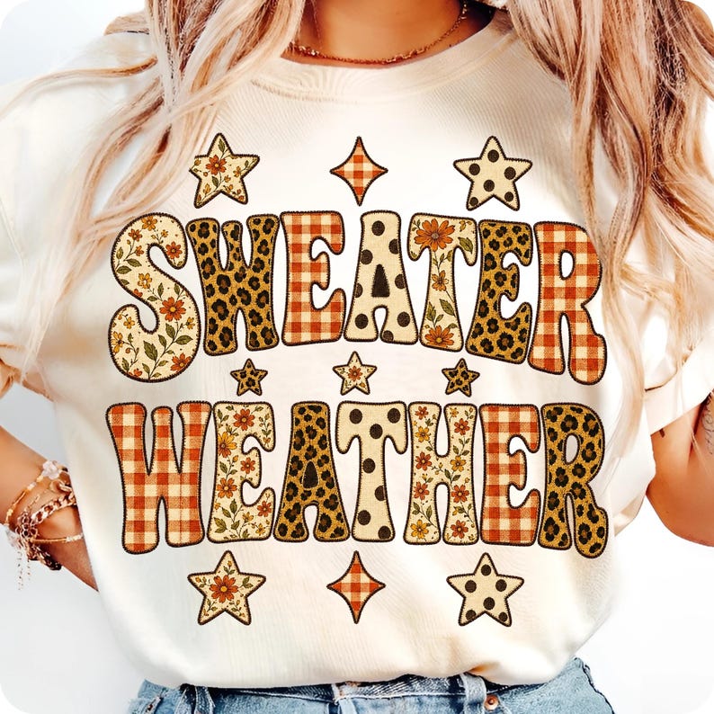 May include: A cream-colored t-shirt featuring the text "SWEATER WEATHER" in large, bold letters. Each letter is filled with a variety of patterns including orange plaid, leopard print, polka dots, and floral designs, accented by small star shapes.