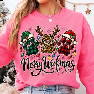 Pu&ograve; includere: Una felpa rosa acceso con una grafica di tre impronte di zampe. La zampa sinistra &egrave; a quadri verdi con un cappello da Babbo Natale, quella centrale &egrave; leopardata con corna di renna e la destra &egrave; a quadri rossi con un cappello da Babbo Natale. Testo Merry Woofmas.