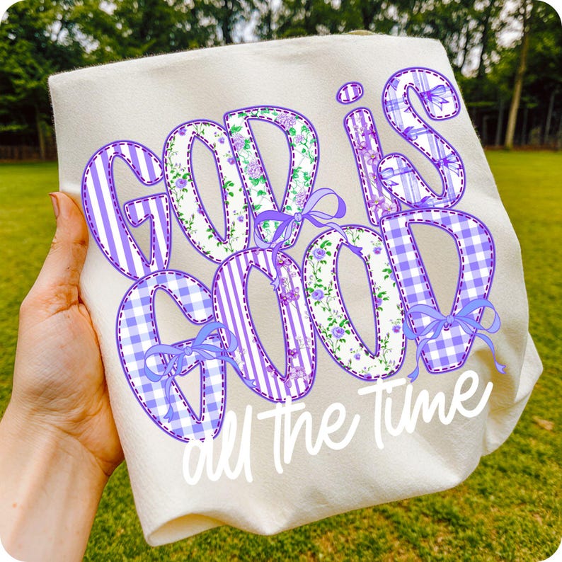 K&ouml;nnte beinhalten: Cremefarbenes Sweatshirt mit dem Schriftzug "GOD IS GOOD all The Time" in einem Patchwork-Design. Die Buchstaben weisen Blumen-, Streifen- und Vichy-Muster in Lila und Wei&szlig; auf, akzentuiert mit lila Schleifen.