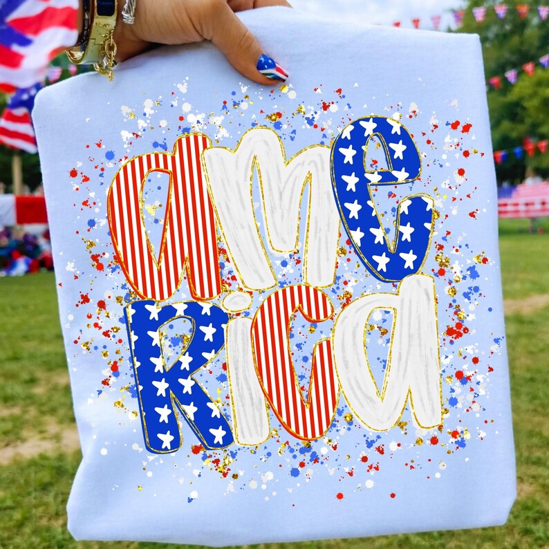 K&ouml;nnte beinhalten: Hellblaues Sweatshirt mit dem Wort "AMERICA" in einem patriotischen Design. Die Buchstaben sind wei&szlig;, rot und blau mit goldenen Akzenten und Sterndetails. Rote, wei&szlig;e und blaue Spritzer sind &uuml;ber das Sweatshirt verstreut.