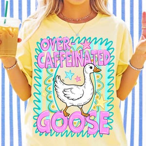 Pu&ograve; includere: Una t-shirt giallo pallido con la grafica di un'oca bianca centrata all'interno di una cornice decorativa color ottanio e oro. Il testo "OVER-CAFFEINATED GOOSE" &egrave; stampato in grandi lettere rosa sopra e sotto l'oca, con piccole stelle decorative.