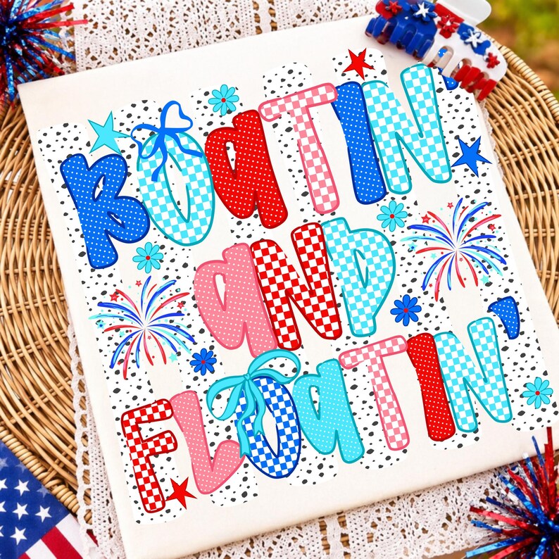 Op de afbeelding: Een wit t-shirt met de tekst "BOATIN AND FLOATIN" in een speels, meerkleurig lettertype met rode, blauwe en roze ruitjes- en stippenpatronen. Het ontwerp bevat kleine blauwe bloemetjes, rode sterren en afbeeldingen van vuurwerk.