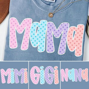 Puede incluir: Una camiseta azul con la palabra "Mama" en letras grandes y coloridas con lunares. Las letras est&aacute;n delineadas en blanco y rellenas con lunares rosas, azules y morados. Se ve un collar dorado con un colgante.