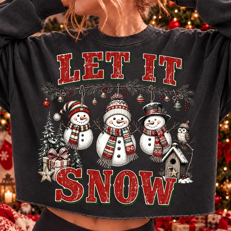 Pu&ograve; includere: Una felpa grigio antracite con la grafica di tre pupazzi di neve che indossano sciarpe e cappelli, con la scritta LET IT SNOW in rosso. Il design include un albero di Natale, un pacco regalo, una casetta per uccelli e un gufo con decorazioni.