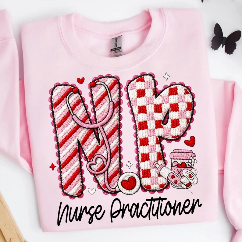 May include: Pink sweatshirt with a graphic design featuring the letters "NP" in red and white, a stethoscope, hearts, and the words "Nurse Practitioner". The design is surrounded by a scalloped border.