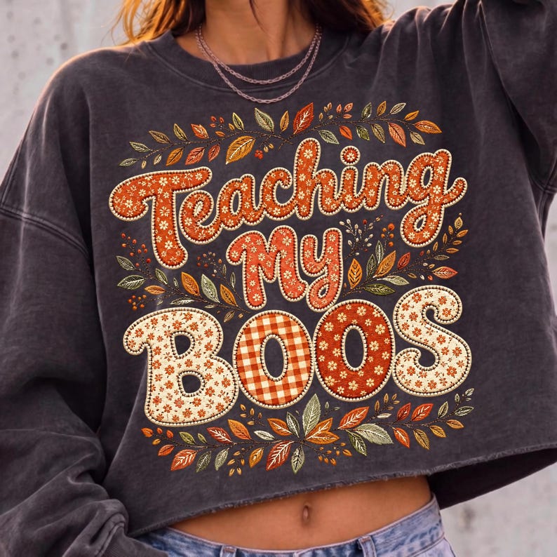 Pu&ograve; includere: Una felpa girocollo grigio antracite con la scritta Teaching My BOOS in grandi lettere decorative a motivi. Il design &egrave; circondato da una colorata disposizione di foglie autunnali nelle tonalit&agrave; dell'arancione, del giallo e del marrone.