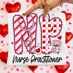 May include: White t-shirt with the letters "NP" in red and pink, featuring a stethoscope design. The shirt also has the words "Nurse Practitioner" in black script, along with hearts and stars. The design is surrounded by a scalloped border.