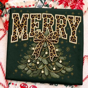 Op de afbeelding: Een donkergroen sweatshirt met het woord MERRY in grote blokletters met een luipaardprint. Onder de tekst staat een geborduurde kerstboom versierd met gouden kralenslingers, kleine witte kerstballen en een strik met luipaardprint.