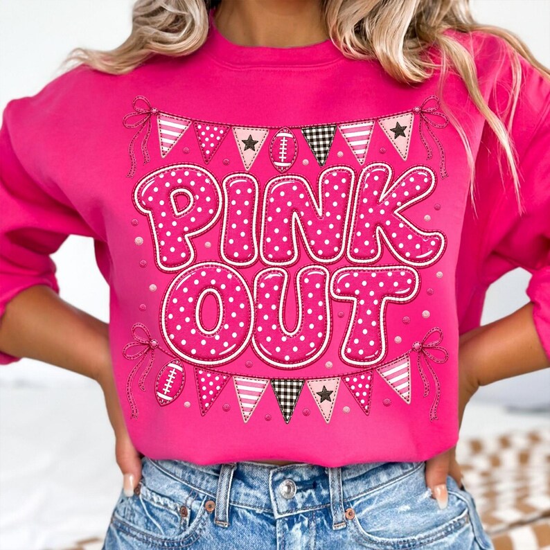 K&ouml;nnte beinhalten: Ein leuchtend pinkfarbenes Langarm-Sweatshirt mit dem Schriftzug PINK OUT in gro&szlig;en, wei&szlig; gepunkteten pinken Buchstaben. Das Design enth&auml;lt eine dekorative Wimpelkette mit Fu&szlig;b&auml;llen, Sternen und Karomustern in Pink, Wei&szlig; und Schwarz.