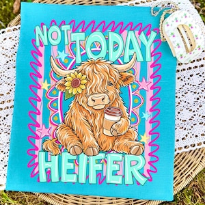 May include: A turquoise tea towel with the words "NOT TODAY HEIFER" in teal and pink. The towel features a cartoon illustration of a Highland cow with a sunflower and a coffee cup. The cow is brown and tan with long shaggy hair.