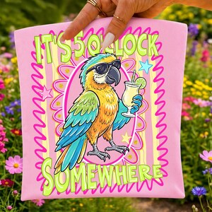 May include: Pink square pillow with a cartoon parrot wearing sunglasses and holding a cocktail. The text "IT'S 5 O'CLOCK SOMEWHERE" is in green and yellow. The parrot is yellow, blue, and orange.