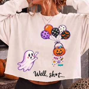 May include: A cream-colored long-sleeve sweatshirt featuring a graphic of a white ghost and a pumpkin-shaped candy bucket held by a cluster of colorful balloons. The text "Well, sh*t..." is printed in black below the graphic illustration.