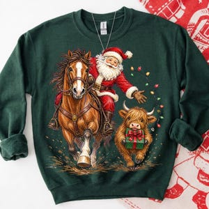 Puede incluir: Una sudadera de cuello redondo verde oscuro con una ilustraci&oacute;n gr&aacute;fica de Santa Claus montando un caballo marr&oacute;n, acompa&ntilde;ado por una peque&ntilde;a vaca Highland que sostiene un regalo verde con un lazo rojo, rodeado de luces navide&ntilde;as de colores.
