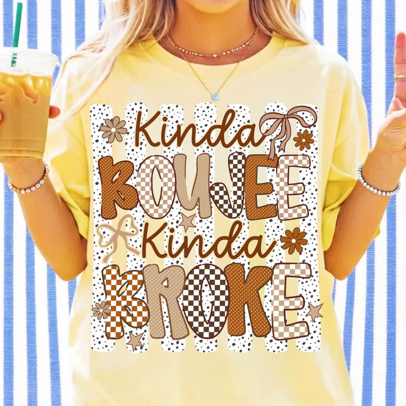 Pode incluir: Uma t-shirt amarelo-p&aacute;lido com uma estampa gr&aacute;fica de riscas verticais e pontos. O texto Kinda BOUJEE Kinda BROKE apresenta padr&otilde;es de xadrez e pontos em castanho e bege, acentuado com flores, estrelas e la&ccedil;os de fita castanhos.