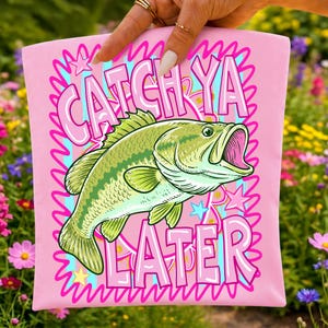 May include: A light pink fabric item featuring a green fish illustration in the center. The text CATCH YA LATER is printed in large, bold pink letters above and below the fish. The design includes a bright pink squiggly border and stars.
