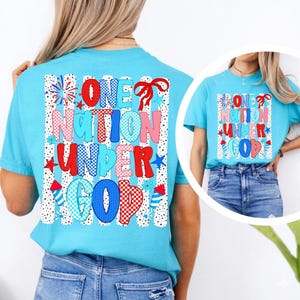 Pu&ograve; includere: Una t-shirt turchese brillante con una stampa grafica che riporta il testo ONE NATION UNDER GOD. Il design include motivi rossi, bianchi e blu, stelle, fuochi d'artificio e un fiocco su uno sfondo a righe verticali con pois neri e bianchi.