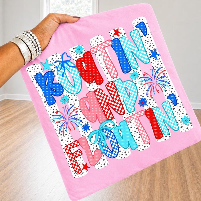 Op de afbeelding: Een vierkante roze kussensloop met de tekst "BOATIN' AND FLOATIN'" in grote, veelkleurige letters met patronen. Het ontwerp bevat rood, blauw en lichtblauw geblokte en gestippelde patronen, kleine sterretjes, bloemen en vuurwerk.
