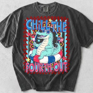 May include: A charcoal gray t-shirt featuring a graphic of a light blue alligator wearing star-shaped sunglasses, sitting in a red, white, and blue striped inner tube while holding a popsicle. The text reads CHILL THE FOURTH OUT.