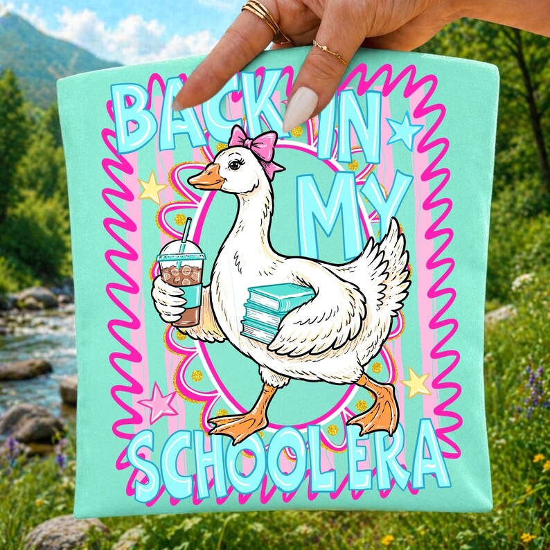 May include: A light teal tote bag featuring a cartoon goose with a pink bow, holding a coffee and books. The text on the bag reads "BACK IN MY SCHOOLERA" in blue and pink. The design is surrounded by a pink wavy border and stars.