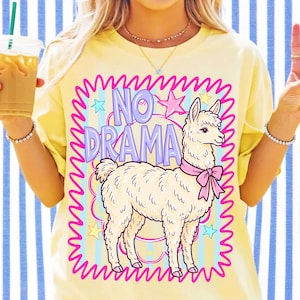 Peut inclure: Un t-shirt jaune p&acirc;le avec un motif repr&eacute;sentant un lama cr&egrave;me portant un n&oelig;ud rose. Le design inclut le texte NO DRAMA en lettres violettes, entour&eacute; d'une bordure rose vif ondul&eacute;e, d'&eacute;toiles bleues et jaunes, et de rayures bleu clair.