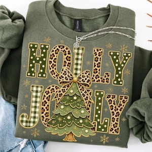 May include: An olive green crewneck sweatshirt featuring the text HOLLY JOLLY in a mix of leopard print, green polka dot, and green gingham patterns. A central graphic shows a stylized green Christmas tree topped with a leopard print bow.