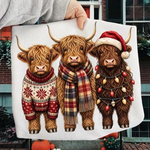 May include: A white fabric featuring a graphic illustration of three brown Highland cows. The left cow wears a red and white snowflake sweater. The middle cow wears a plaid scarf. The right cow wears a red Santa hat and a string of colorful Christmas lights.