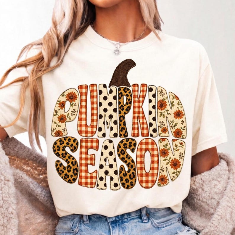 以下が含まれることがあります： クリーム色の半袖Tシャツで、PUMPKIN SEASONという文字が書かれたカボチャの形の大きなグラフィックが特徴です。文字はオレンジ色のチェック柄、黒い水玉模様、ヒョウ柄、ヒマワリなど、さまざまなパターンで装飾されています。