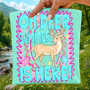 Może przedstawiać: Jasnozielony kwadrat z tkaniny z centralną ilustracją płowego jelenia. Tekst brzmi OH DEER SUMMER IS HERE pogrubionymi niebieskimi literami. Projekt zawiera r&oacute;żową falistą obw&oacute;dkę, ż&oacute;łte i niebieskie gwiazdki oraz r&oacute;żowe paski.