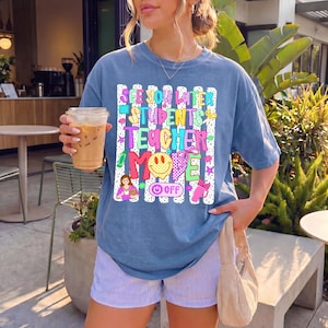 K&ouml;nnte beinhalten: Ein blaues Kurzarm-T-Shirt mit einem Grafikdruck aus wei&szlig;en vertikalen Streifen und buntem Text mit der Aufschrift "SEE YOU LATER STUDENTS TEACHER MODE OFF". Das Design enth&auml;lt ein gelbes Smiley-Gesicht, einen Stift und eine Lehrer-Illustration.