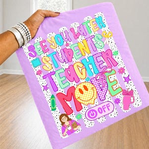 K&ouml;nnte beinhalten: Ein hellvioletter Stoffartikel mit einem bunten Grafikdruck und dem Text "SEE YOU LATER STUDENTS TEACHER MODE OFF". Das Design enth&auml;lt ein gelbes Smiley-Gesicht, einen gr&uuml;nen Buntstift, einen rosa Becher und eine Lehrer-Illustration.