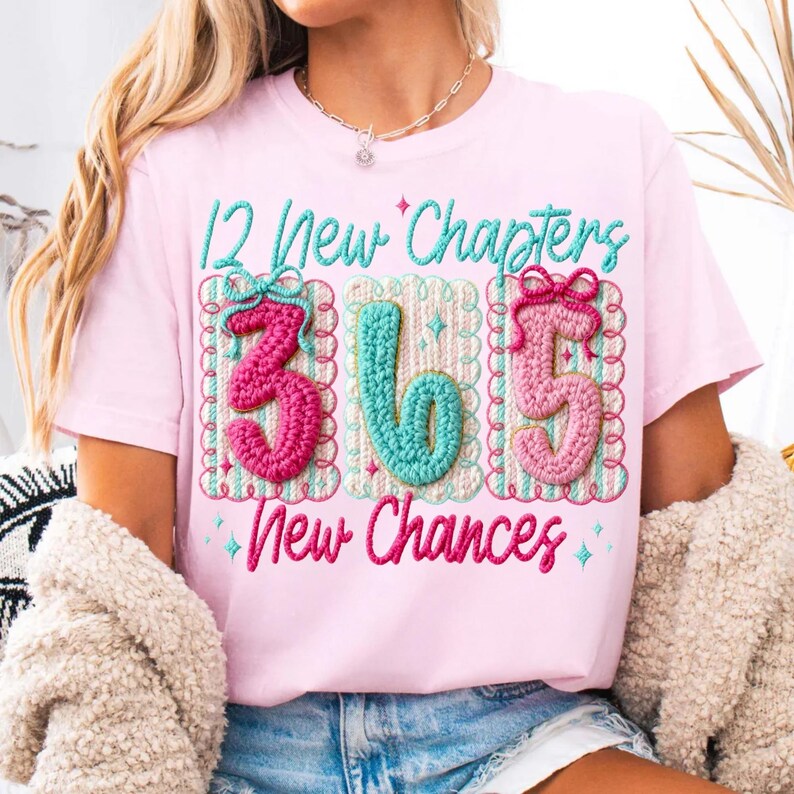 Puede incluir: Camiseta rosa claro con el texto bordado "12 New Chapters 365 New Chances". Los n&uacute;meros y el texto son en rosa, turquesa y blanco. La camiseta tiene cuello redondo y es de estilo casual.