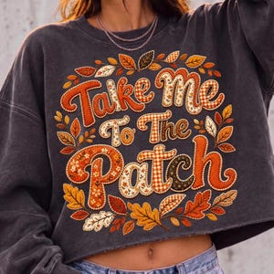 May include: A charcoal gray cropped sweatshirt featuring the text Take Me To The Patch in large, stylized letters. The lettering is filled with various orange, brown, and white patterns, surrounded by a wreath of colorful autumn leaves.